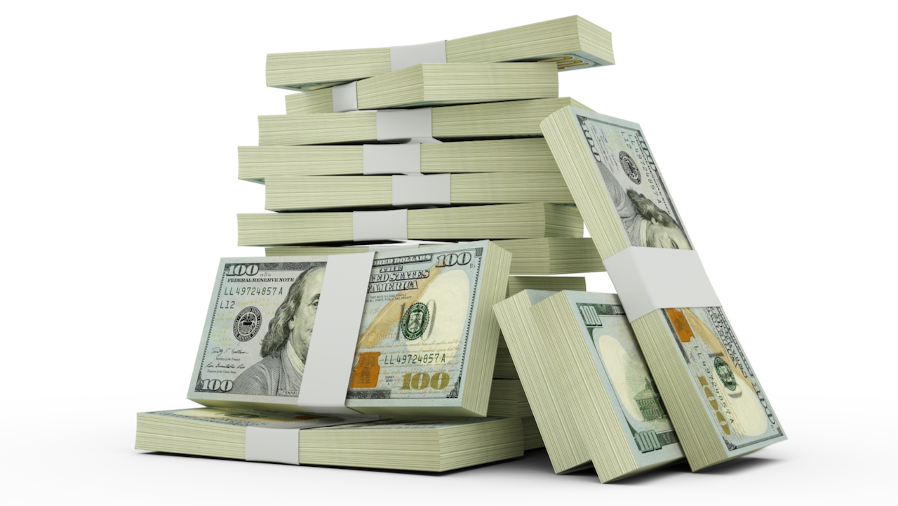 Stacks of $100 US dollar bills arranged in piles, with some bundles leaning against each other, set against a white background.