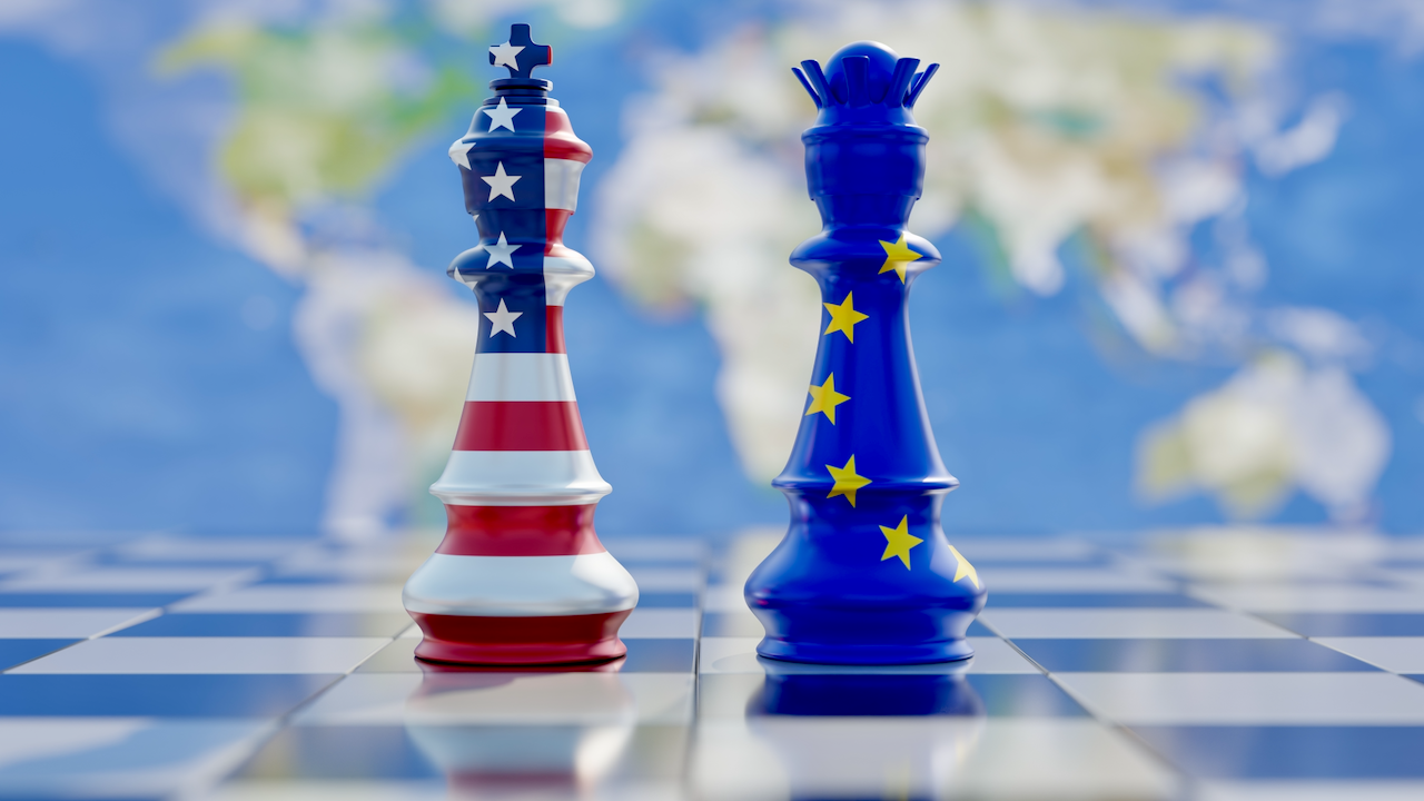 Two chess pieces, a king with the American flag design and a queen with the European Union flag design, stand on a chessboard with a blurred world map in the background.