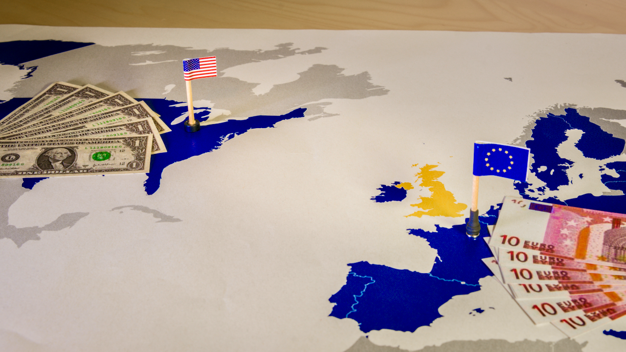 A map showing the US and Europe with small flags, US flag by dollar bills and EU flag by euro notes, symbolizing financial relations between the regions.