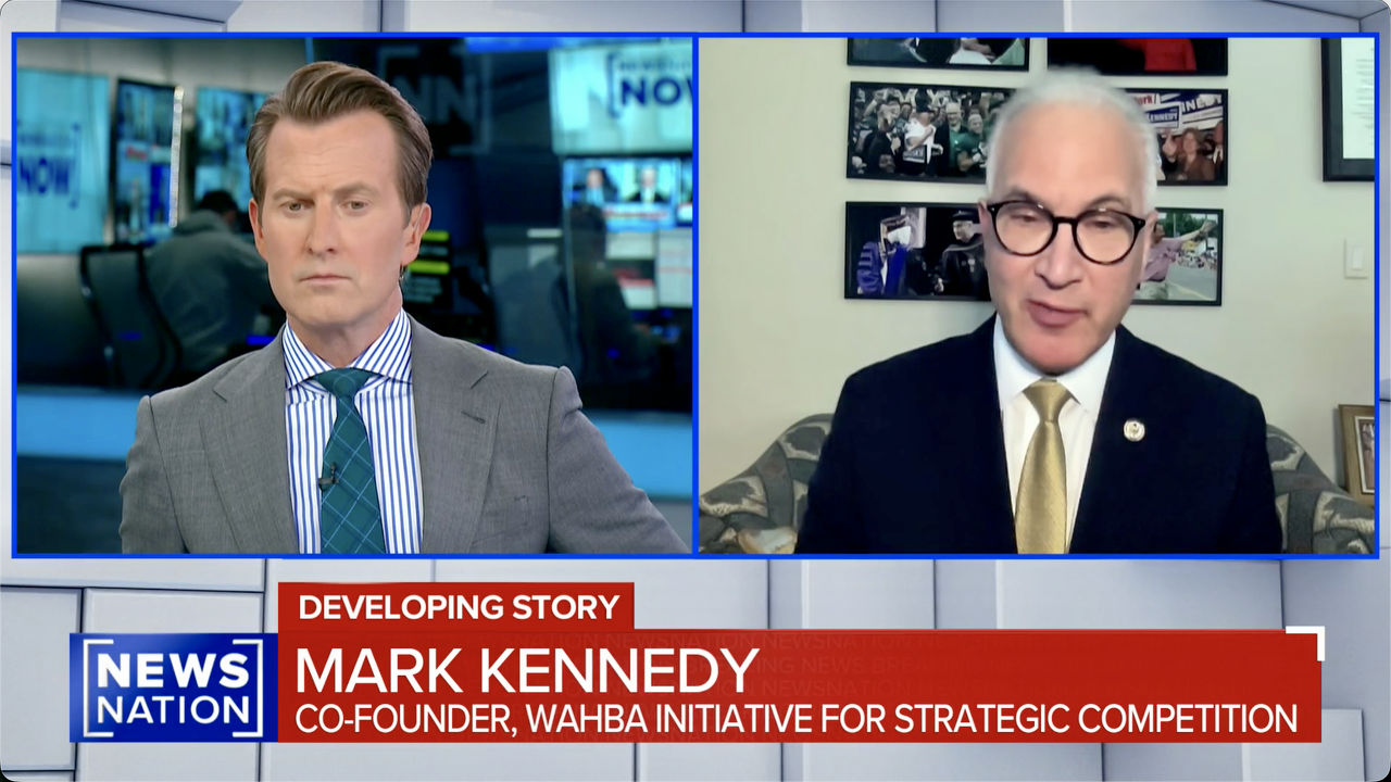 Split-screen news interview: a serious male anchor on the left listens to Mark Kennedy, wearing glasses and a suit, on the right. News graphic reads “Developing Story — Mark Kennedy, Co-Founder, Wahba Initiative for Strategic Competition.”.