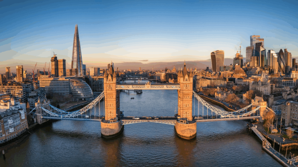 Aerial view of London’s Tower Bridge spanning the River Thames at sunset, with the Shard skyscraper on the left and modern city buildings in the background under a clear sky.