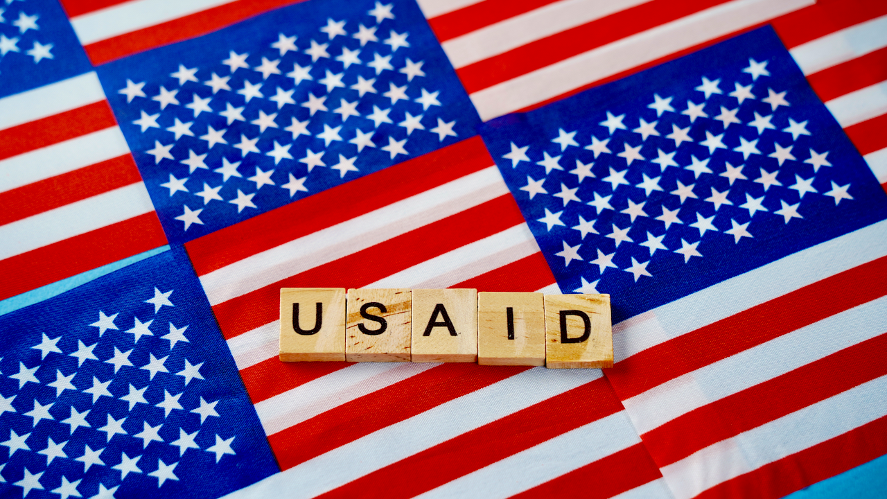 Scrabble tiles spelling USAID are arranged on a background made up of multiple overlapping American flags.