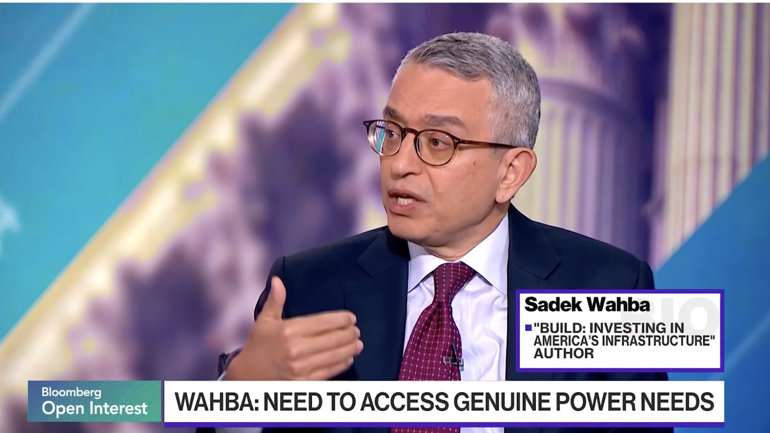 A man in a suit and glasses speaks during a Bloomberg TV interview. The on-screen text identifies him as Sadek Wahba, author of Build: Investing in Americas Infrastructure. The backdrop is blurred.