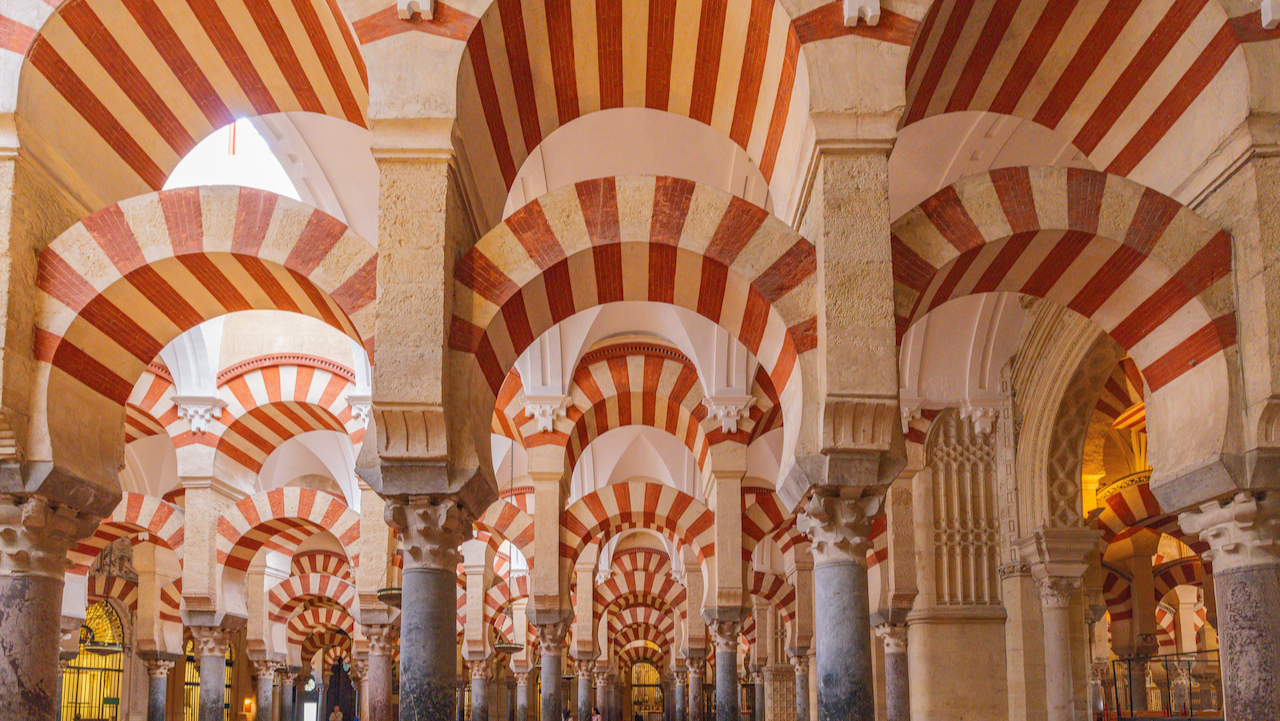 Rows of stone columns topped with red and white striped horseshoe arches inside the Mosque-Cathedral of Córdoba, creating a striking and intricate pattern throughout the historic interior.