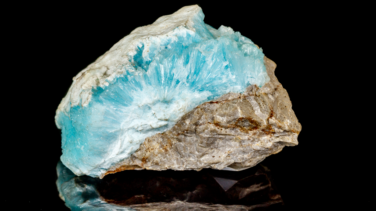 A rough mineral specimen with a striking light blue crystalline formation embedded in a matrix of white and tan rock, displayed against a black background.