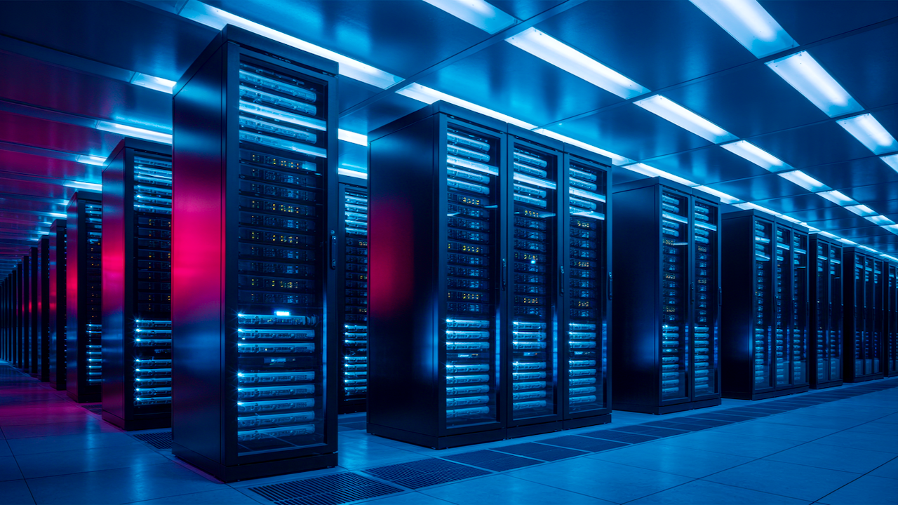 Rows of tall, illuminated server racks stand in a high-tech data center, glowing with blue and red lights under a reflective ceiling, creating a futuristic and organized atmosphere.